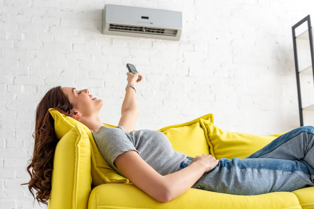 Woman relaxing on couch and using remote control for mini split air conditioning system.